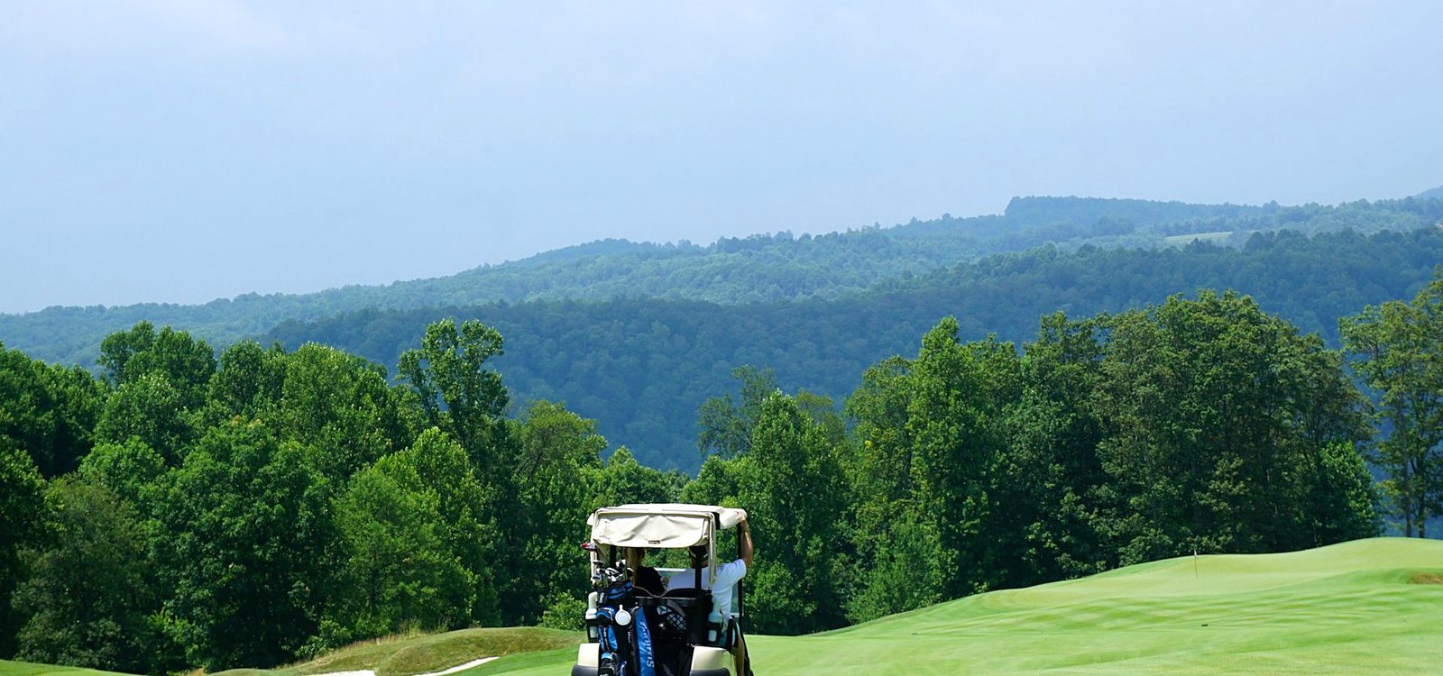 A staff member driving a golf cart along a shaded cart path on the course